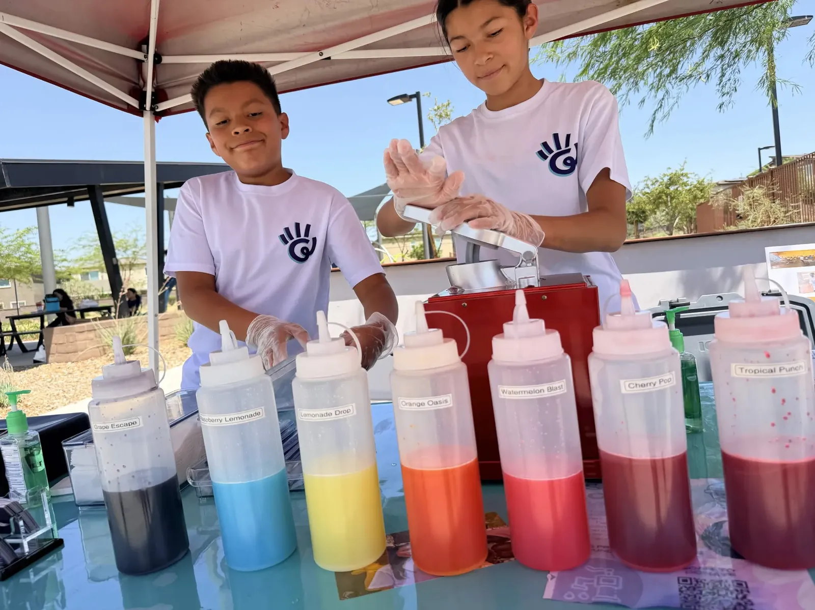 Maya and AT3 making snow cones with a row of flavor syrups